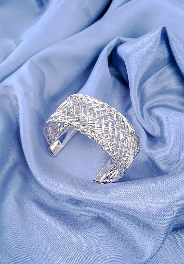 th - 2025-12-12T174739.673 The bracelet features a dense, intricate, and evenly woven mesh pattern made from numerous thin, shiny gold wires, giving it a rich texture. The cuff is open at the bottom.