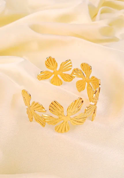 a wide, gold-colored open-cuff bracelet decorated with an array of individual flower motifs