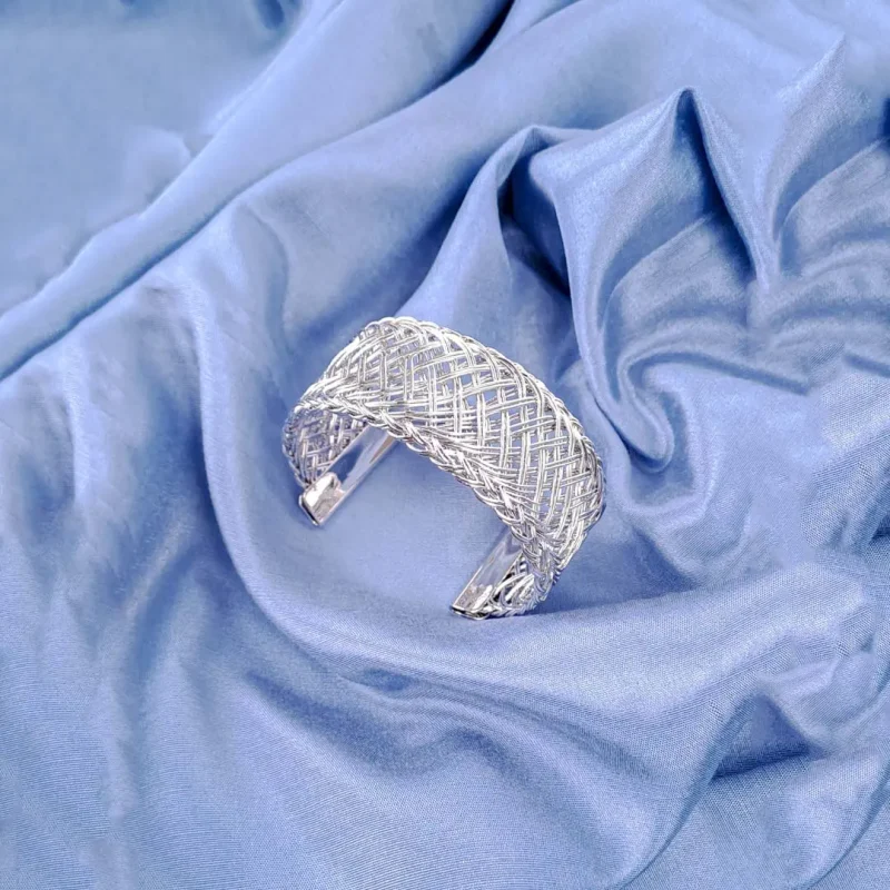 The bracelet features a dense, intricate, and evenly woven mesh pattern made from numerous thin, shiny gold wires, giving it a rich texture. The cuff is open at the bottom.